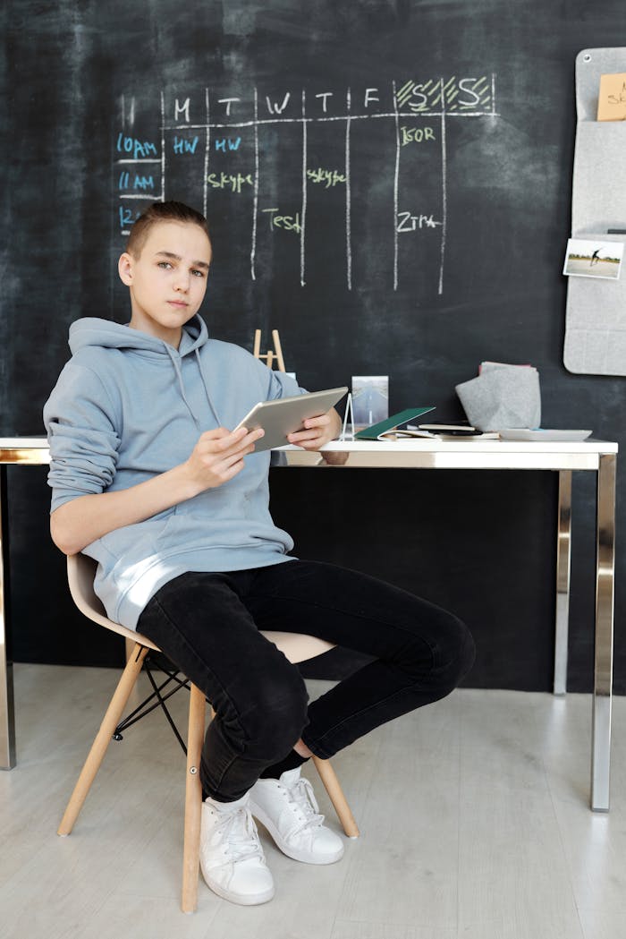 Boy in Gray Hoodie and Black Pants While Sitting on Chair